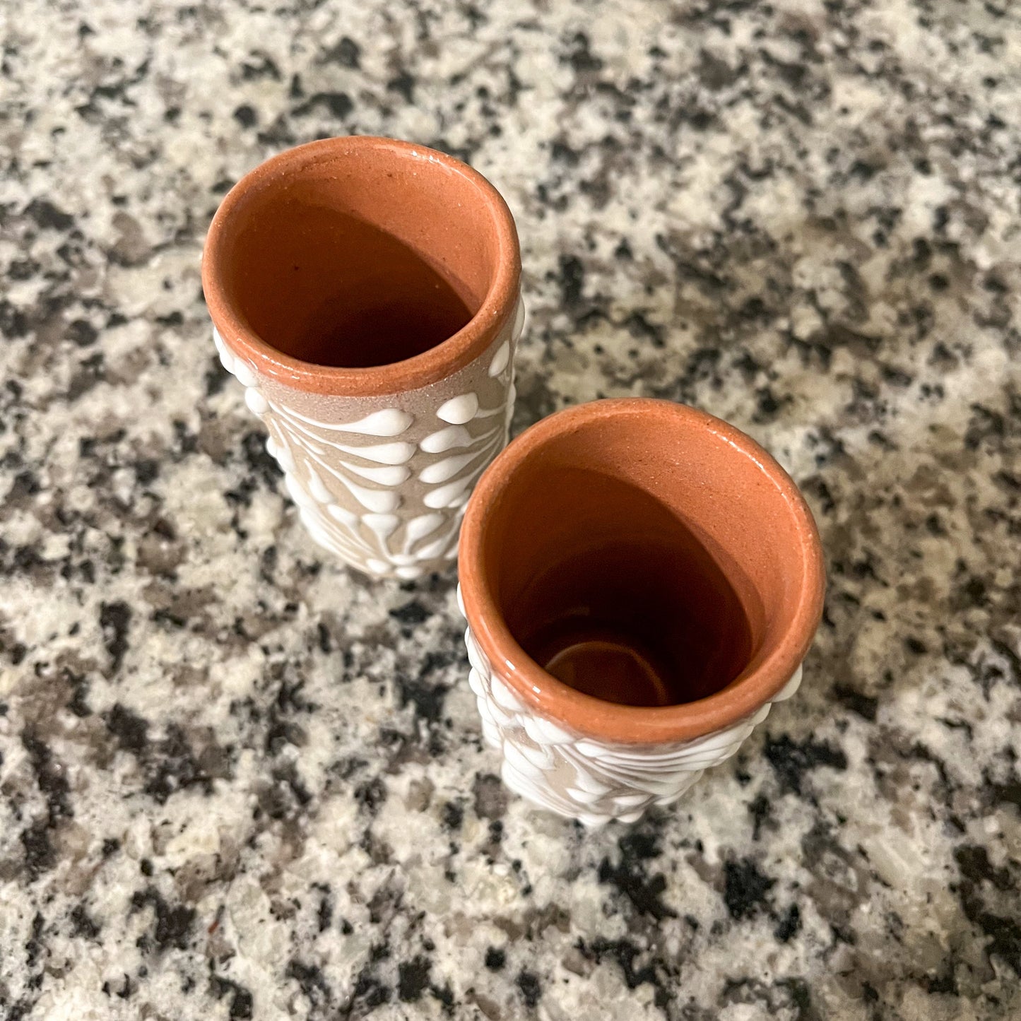 Two shot glasses with decorative patterns on a granite surface