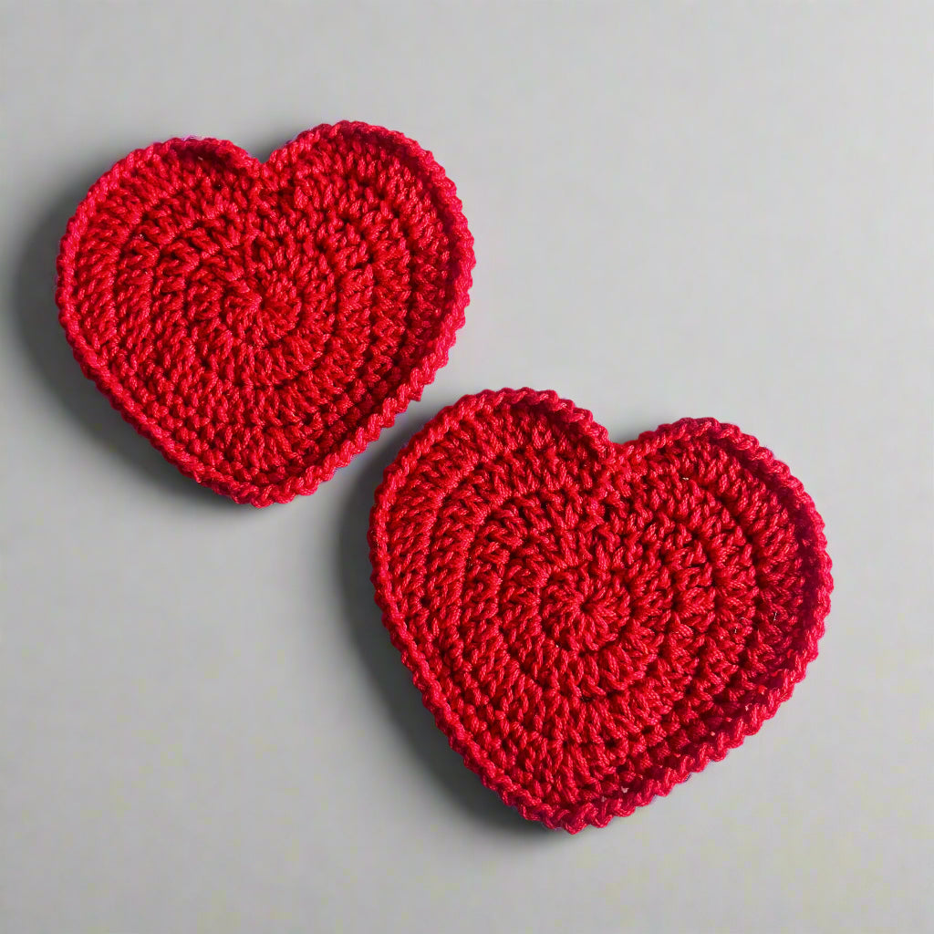 Two red heart-shaped crochet coasters placed on a light background.