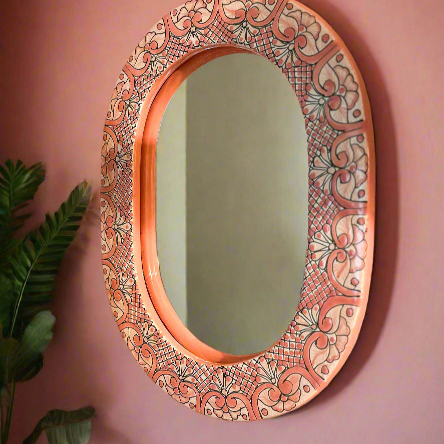Decorative oval mirror with intricate patterns on a pink wall