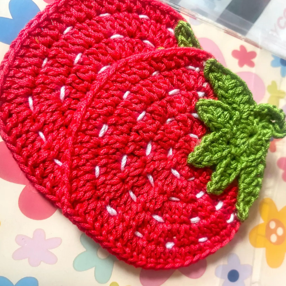 A set of vibrant red and green strawberry-shaped crochet coasters made from cotton, displayed on a white background.