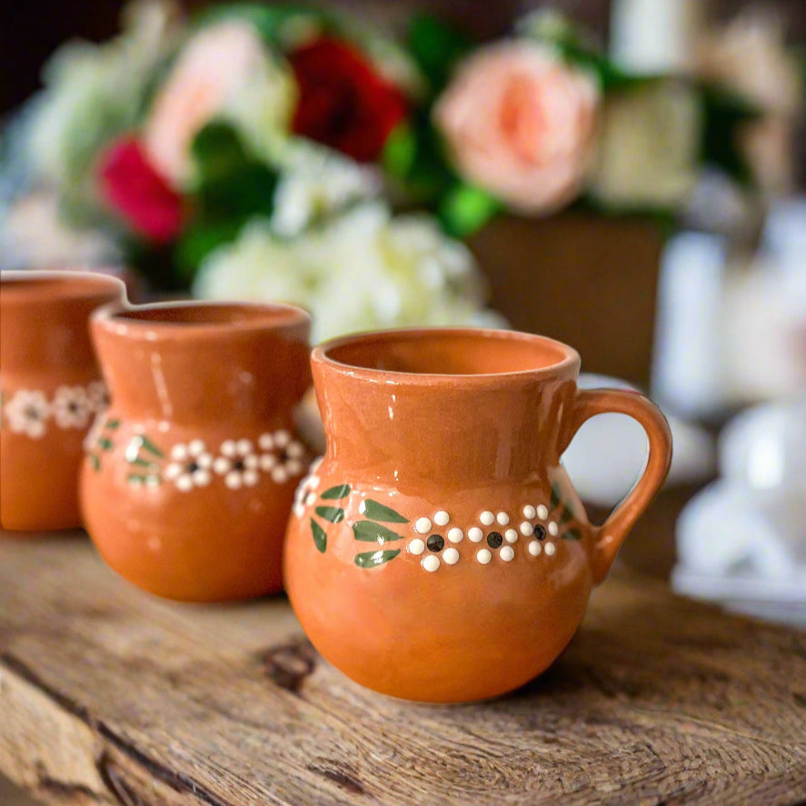 Set of BARRO mugs with decorative patterns on a wooden surface with flowers in the background