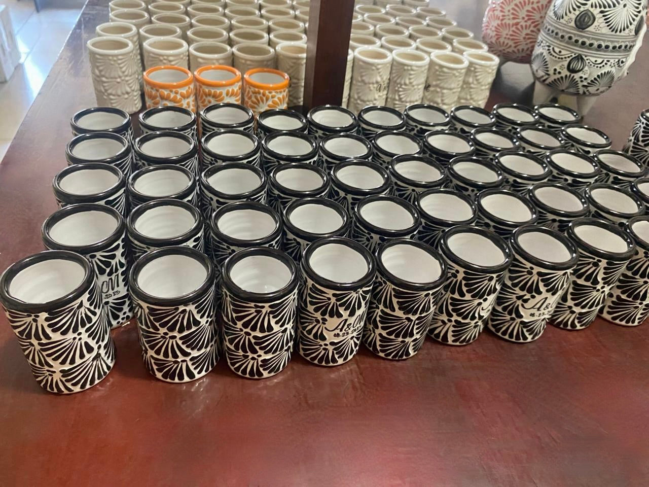 Rows of ceramic shot glass with decorative patterns on a wooden surface.