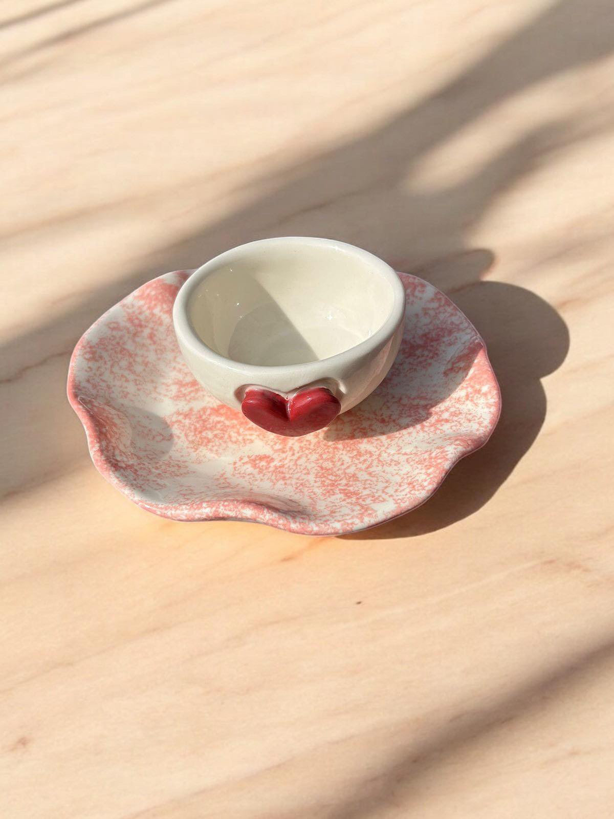 A white ceramic jewelry holder with a heart detail on the front, sitting on a soft pink wavy plate. Ideal for organizing jewelry, such as rings and earrings, this delicate design combines functionality with a charming aesthetic. 💖