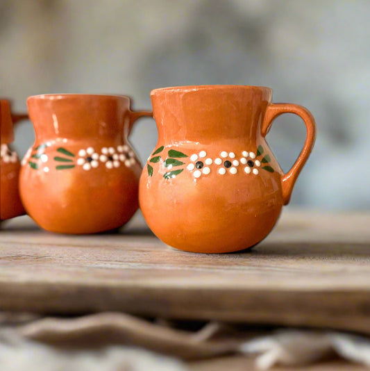 Three terracotta mugs with floral patterns on a wooden surface.