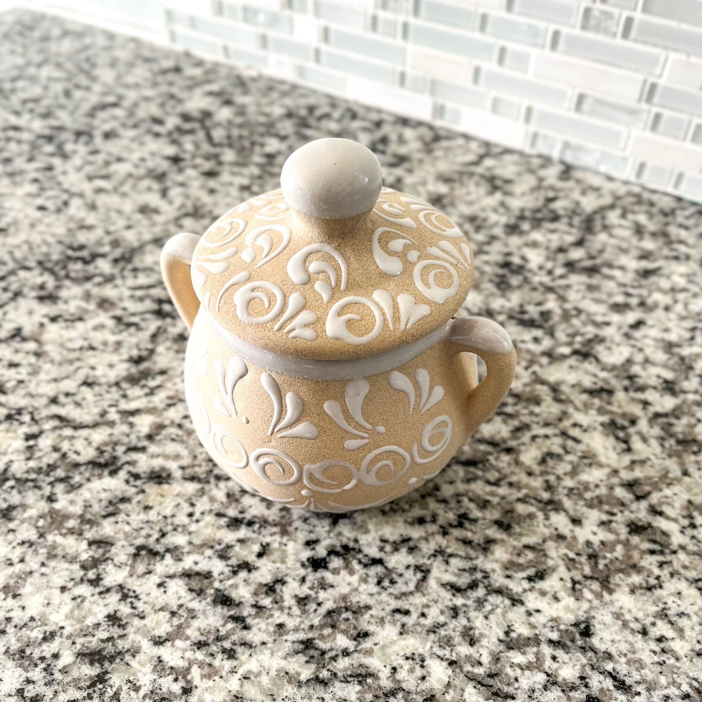 A handmade ceramic sugar bowl with a floral pattern, predominantly beige and pink in color, with a lid and two handles.