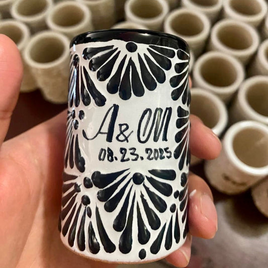 shot glass with black and white pattern held in hand, with stacked containers in the background