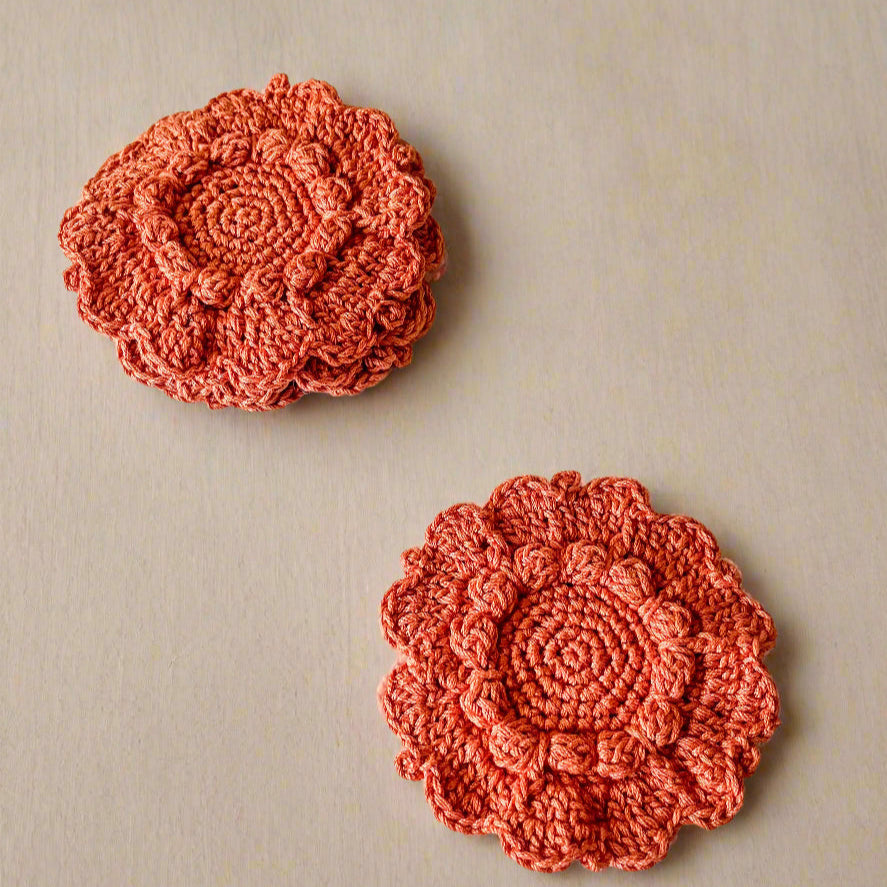 Two crocheted flower coasters on a white textured surface