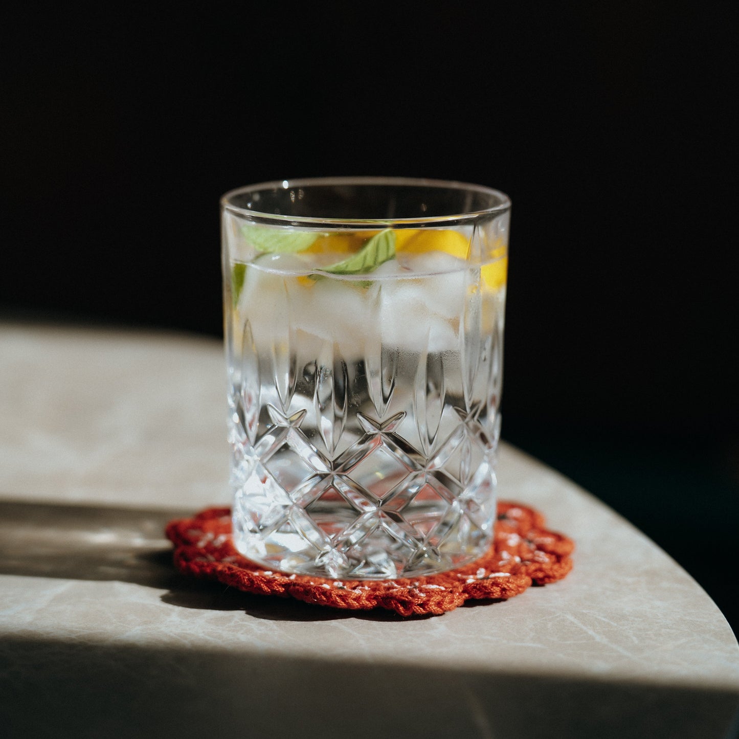 Clear glass with a cocktail on a red coaster on a dark background