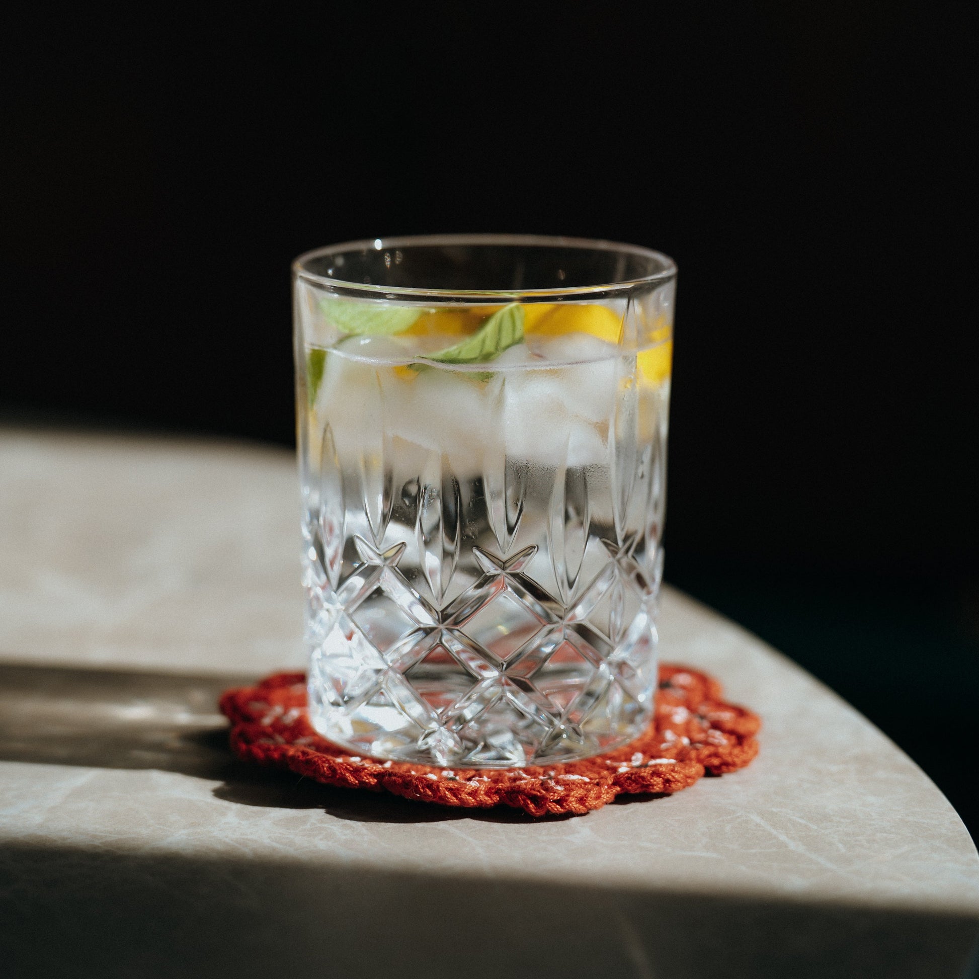 Clear glass with a cocktail on a red coaster on a dark background