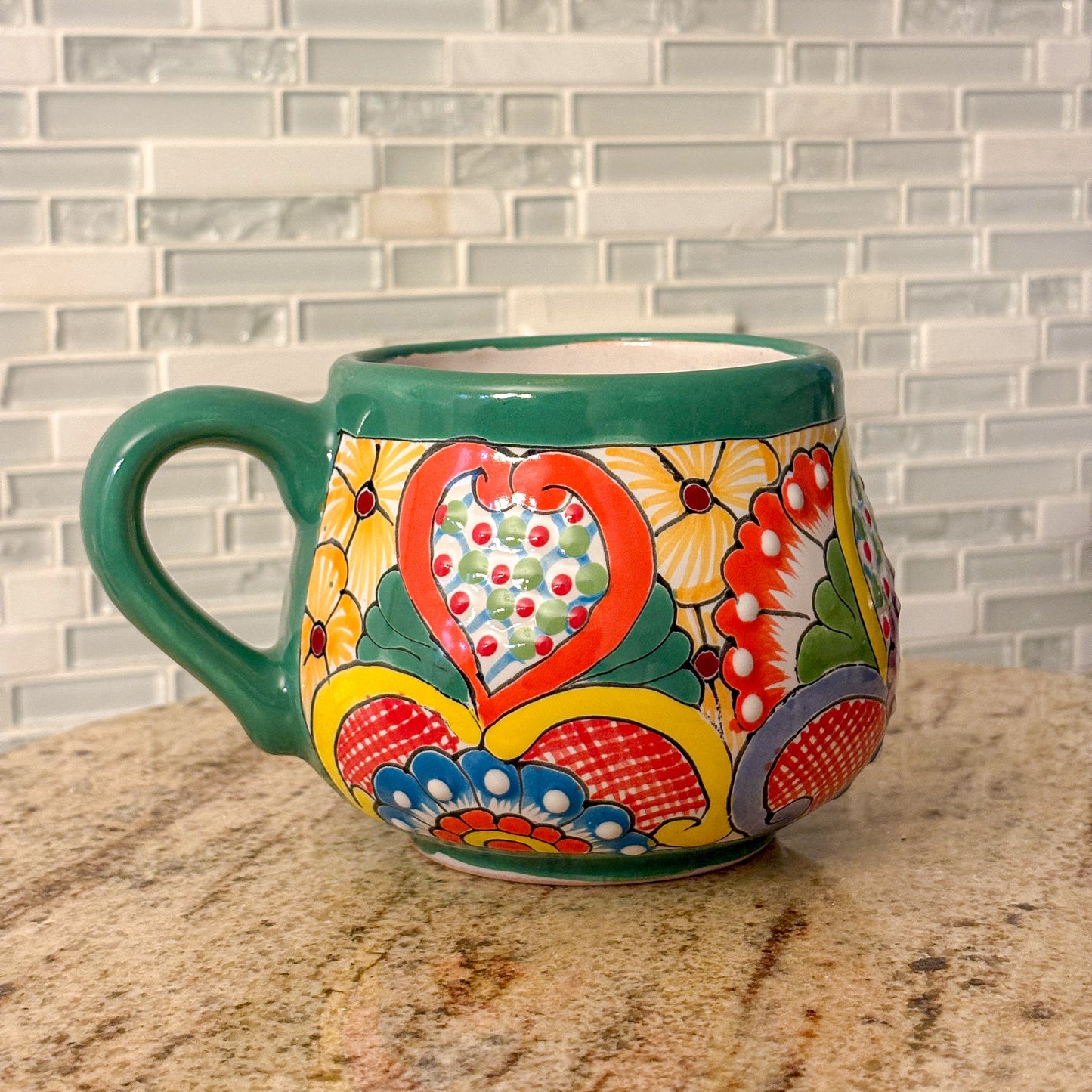 talavera green mug with floral and heart design on a marble countertop with a tiled wall background