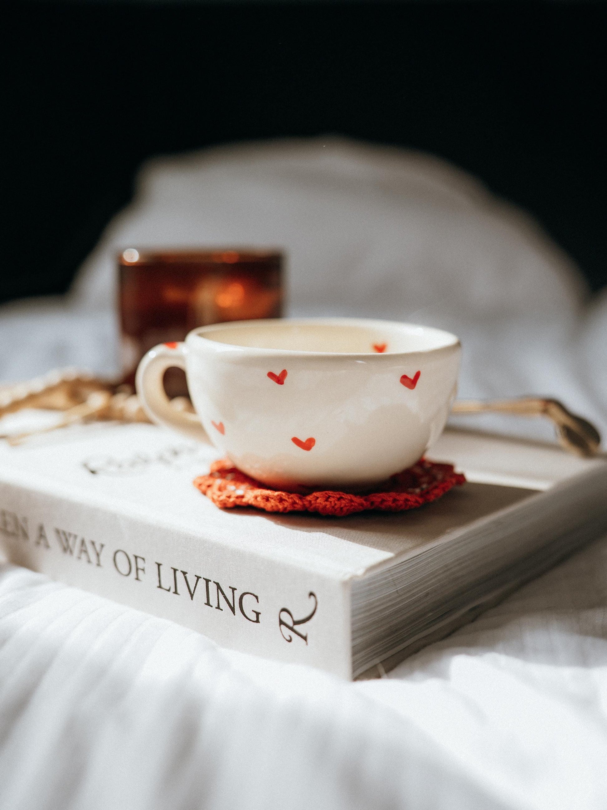 Ceramic heart mug with crochet coaster, book, and lit candle , warm and relaxing setup