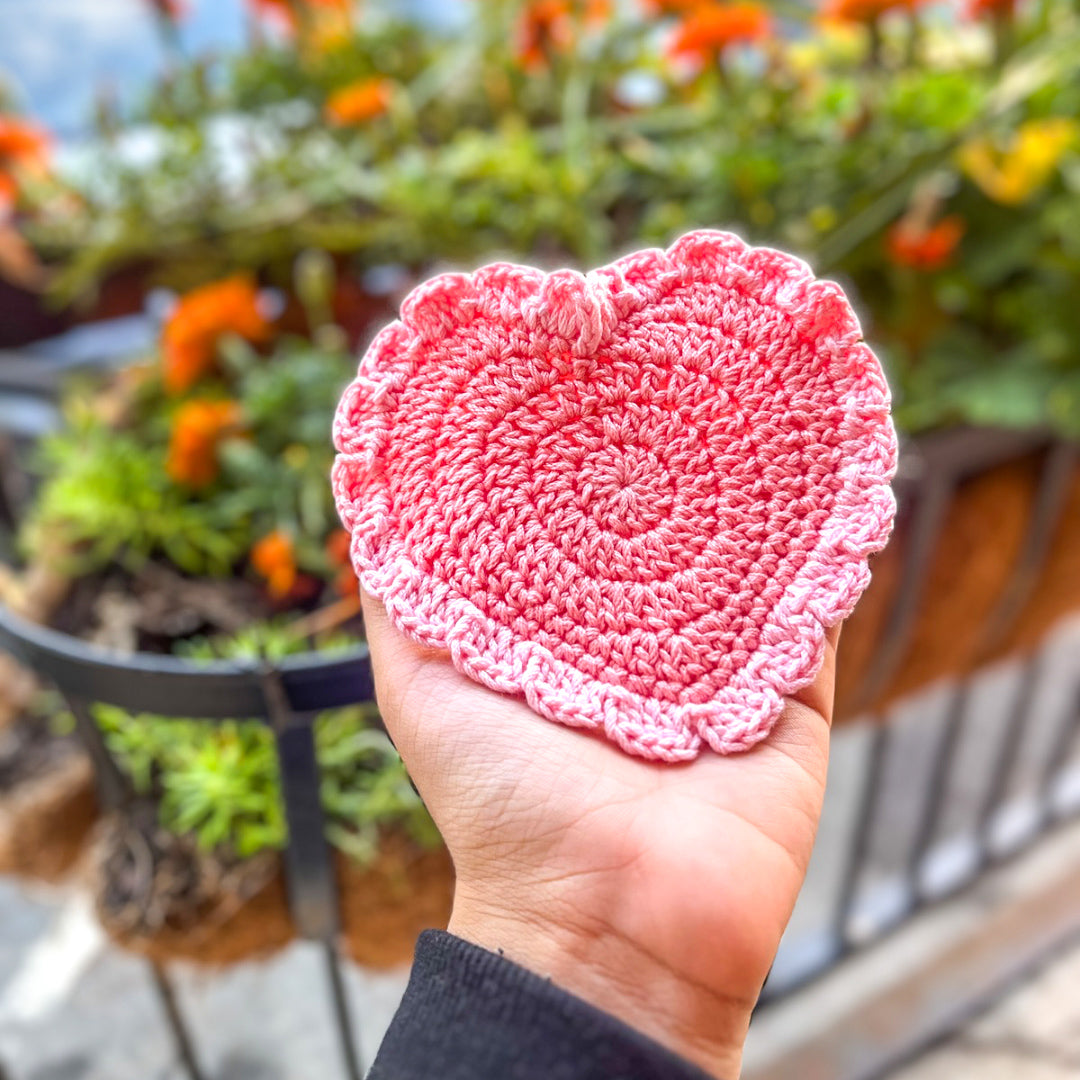 Handmade pink crochet coaster featuring a delicate heart pattern