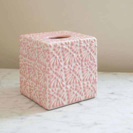 A square pink ceramic tissue box cover with an embossed floral pattern, sitting on a white marble surface against a beige wall.