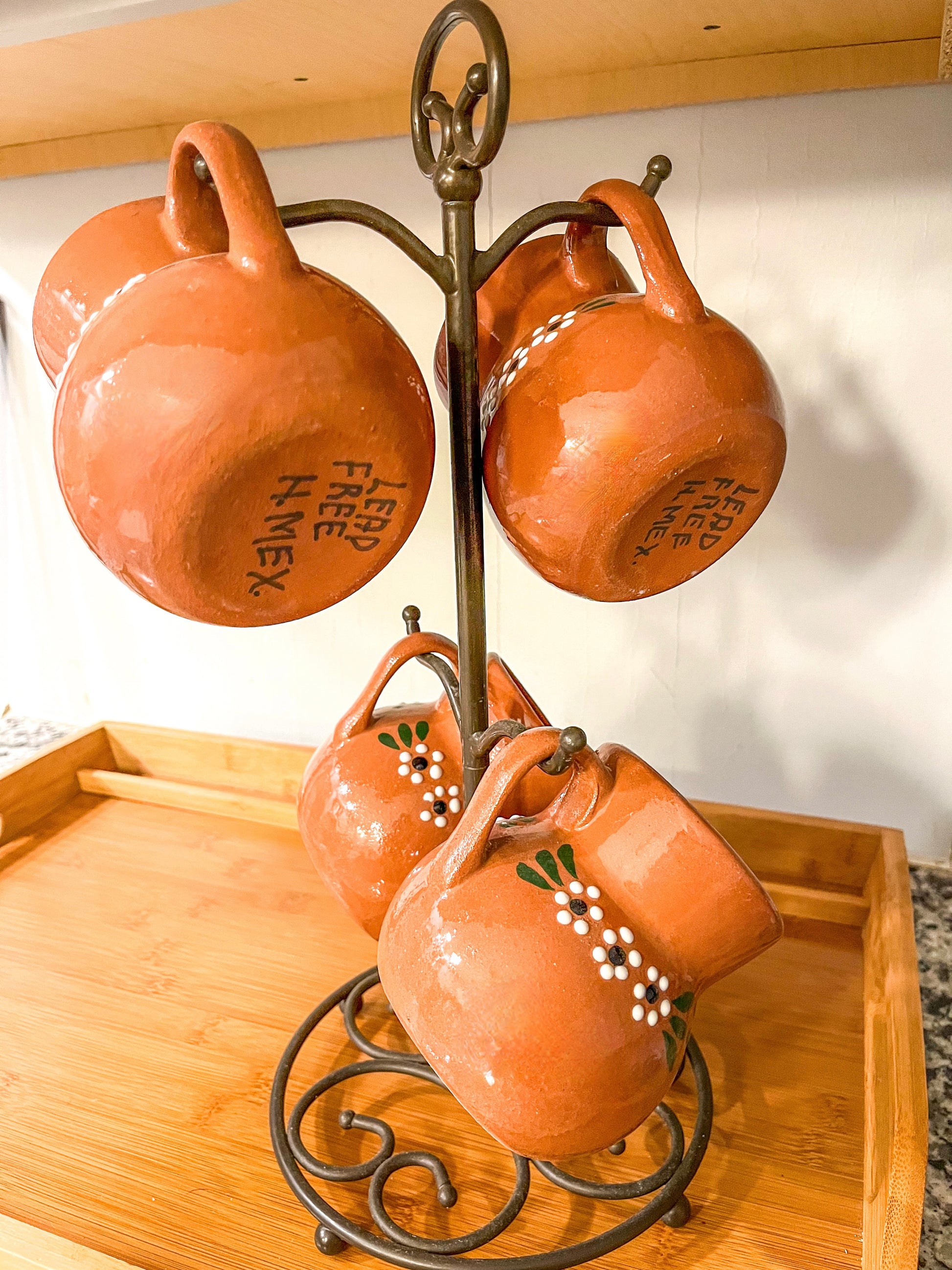 Set of terracotta mugs on a metal stand with a wooden tray below.