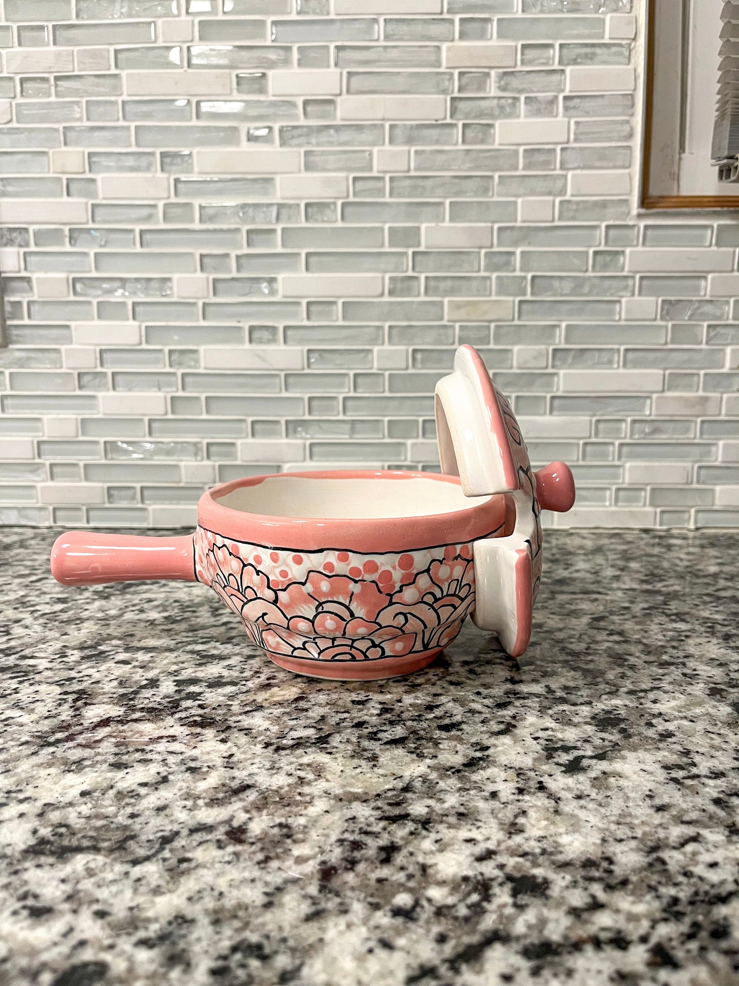 Handmade pink Talavera bowl with the lid off. The bowl is placed on a granite gray countertop, with vibrant floral patterns visible, highlighting its handcrafted beauty.