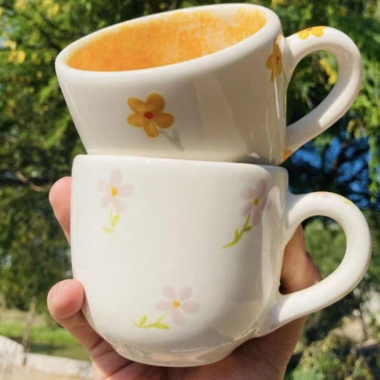 A hand holding two stacked white ceramic mugs with delicate yellow and pink floral patterns, set against an outdoor blurred background. The image is a screenshot from an Etsy Instagram listing showing the product price as $24.